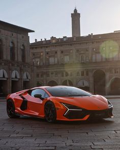 an orange sports car is parked in front of a large building with two towers on each side