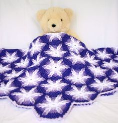 a teddy bear sitting on top of a crocheted blanket in the shape of a flower