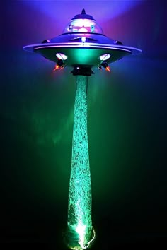 a green and blue light shining on top of a flying saucer