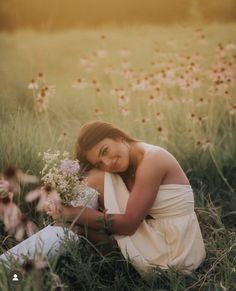 a woman sitting in the middle of a field with flowers on her lap and holding a bouquet