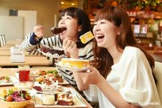 two women sitting at a table with plates of food in front of them and eating