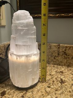 a tall white cake sitting on top of a counter next to a measuring tape