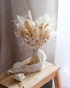 a bouquet of flowers sitting on top of a wooden table next to a white curtain