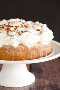 a cake with white frosting and nuts on top sitting on a plate next to a wooden table