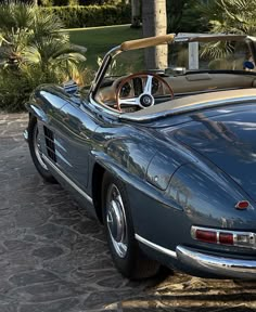 an old blue sports car parked in front of a palm tree