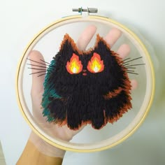 a hand holding a small black cat with glowing eyes in front of a white wall