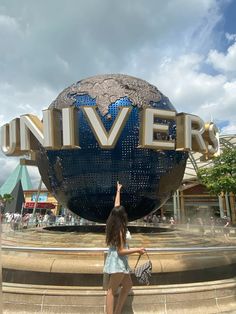 a woman pointing up at the sign for universal studios in front of a building with a giant globe on top