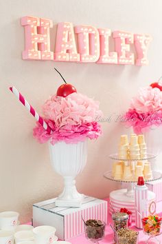 two vases filled with pink flowers and candy on top of a table next to a sign