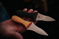 a person holding two knives in their hand, one is black and the other is orange