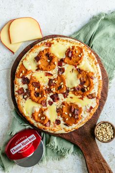 a pizza sitting on top of a wooden cutting board next to an apple and cheese slice