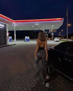 a woman standing in front of a gas station at night with her back to the camera