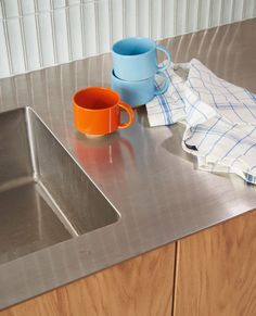 a stainless steel sink with two mugs and a tea towel on the counter top