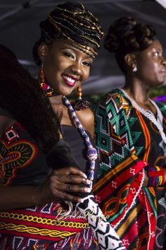 two women in colorful clothing standing under an umbrella