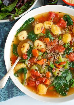 a white bowl filled with vegetable soup next to some bread and salad on a blue table cloth