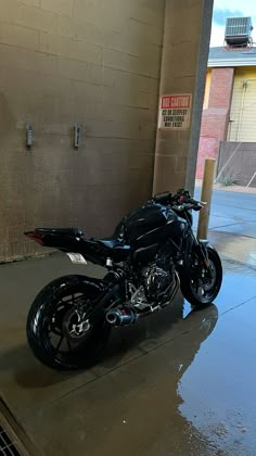 a black motorcycle parked in front of a building on a wet sidewalk next to a parking meter