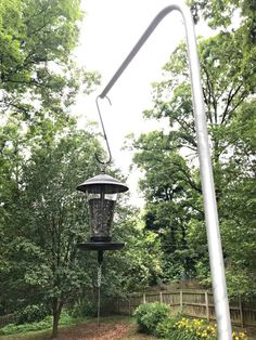 a bird feeder hanging from the side of a metal pole next to trees and flowers