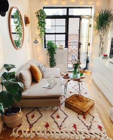 a living room filled with lots of furniture and plants on top of a wooden floor