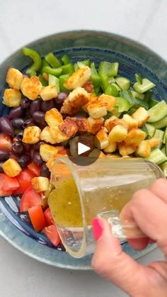 a person pouring dressing into a bowl filled with vegetables and olives to make a salad