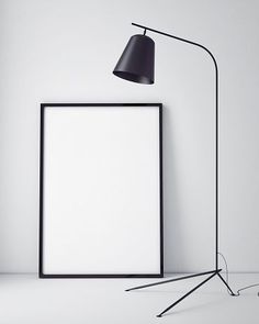 an empty photo frame next to a black floor lamp on a white wall with a black shade