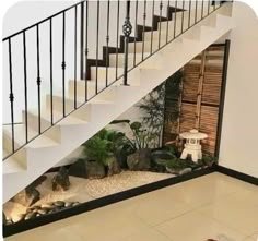 an indoor area with plants and rocks under the stair railing, next to a white staircase