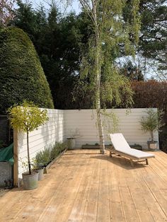 a wooden deck with a white lounge chair next to a small tree and shrubbery