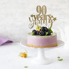 a cake topped with berries on top of a white cake stand next to a purple napkin