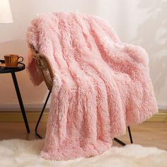 a pink blanket sitting on top of a wooden chair next to a table with a cup