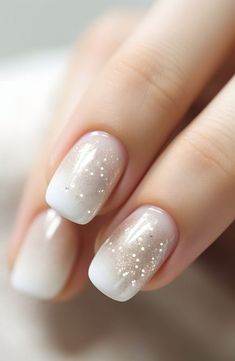 a woman's nails with white and gold glitters on the tip of them