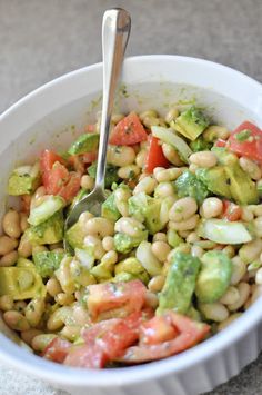 a white bowl filled with lots of veggies and a spoon in the bowl