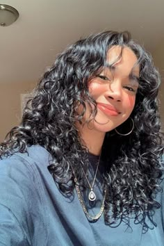 a close up of a person with long curly hair wearing a blue shirt and gold hoop earrings