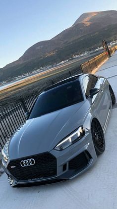 a silver car parked on the side of a road next to a fence and mountains