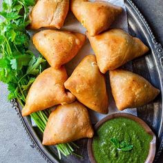 several pastries on a plate with green sauce and parsley next to the pastry