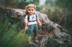 a doll is walking through the grass with a stick in her hand and wearing green pants