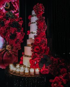 a wedding cake with red flowers and candles on the table in front of a photo