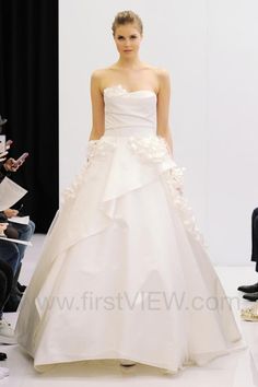 a woman in a white wedding dress standing on a runway with people taking pictures behind her