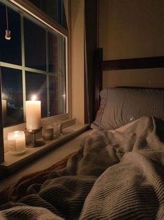 two candles are lit on the window sill in front of an unmade bed