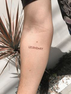 a man's leg with the word legendary tattooed on his left arm, next to a potted plant