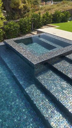 an outdoor swimming pool with blue and green tiles on the floor, surrounded by greenery