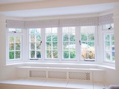 an empty room with three windows and a bench in front of the window, all white