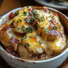 a white bowl filled with potatoes covered in cheese and bacon on top of a wooden table