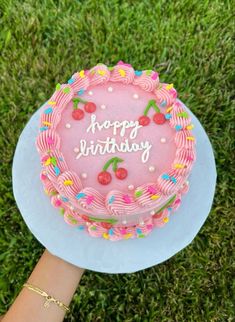 a pink birthday cake sitting on top of a blue plate in the middle of grass