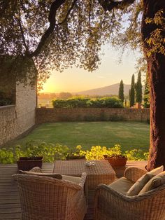 two wicker chairs sitting on top of a wooden deck next to a lush green field