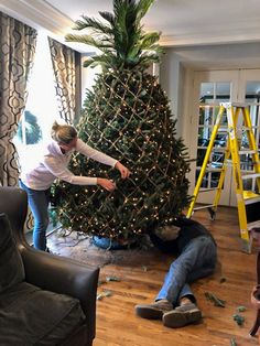 two people decorating a christmas tree in a living room