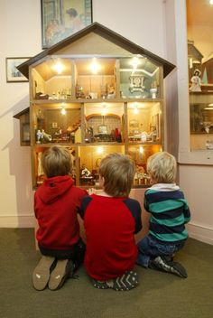 two young boys looking at a doll house in a display case with dolls inside it