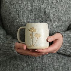 a woman holding a coffee mug with flowers painted on the outside and inside, in her hands