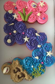 cupcakes decorated with pink, blue and purple icing are arranged in the shape of an e