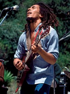 a man with dreadlocks playing guitar in front of a microphone