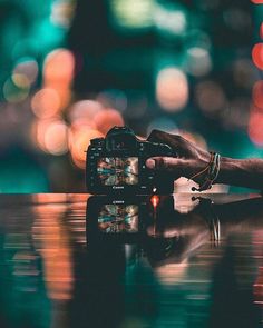 a person holding a camera on top of a table with blurry lights in the background