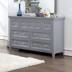 a gray dresser with flowers on top and a mirror in the middle, along with a white rug