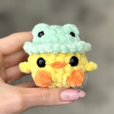 a hand holding a small yellow and green stuffed animal with a hat on it's head